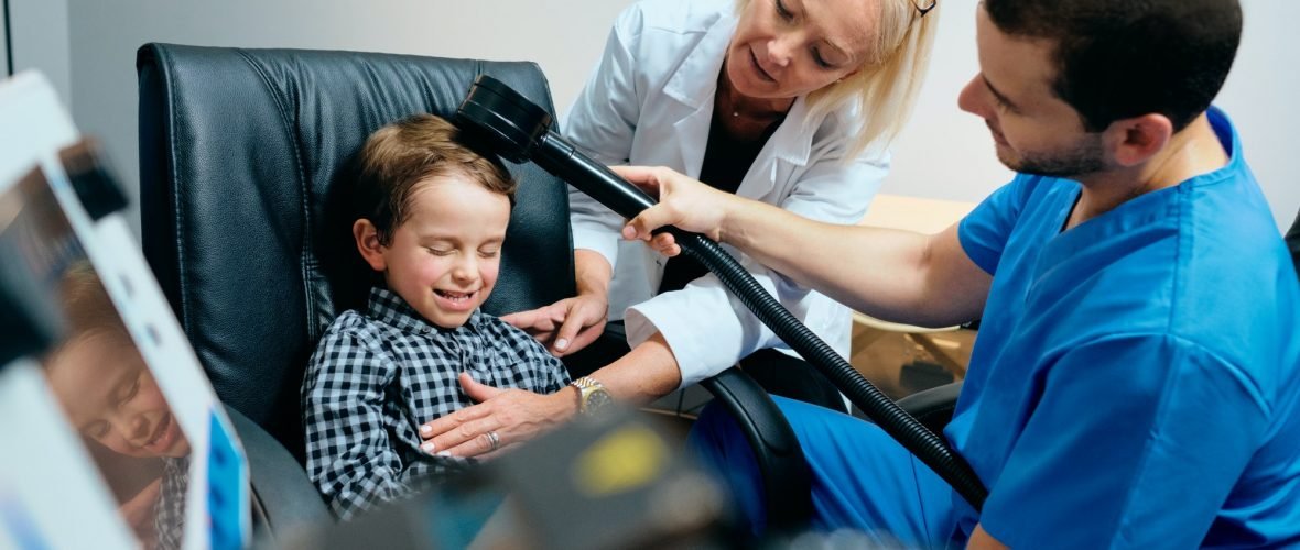 Paediatrician Doctor Doing Brain Treatment To Autistic Child In Clinic